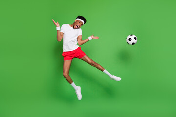 Fototapeta na wymiar Photo of funky active guy jump kick ball wear headband white t-shirt shorts footwear isolated green color background