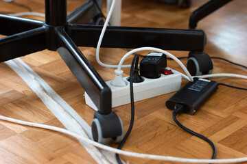 Messy outlet power extension cord on an apartment floor with various charging devices plugged in