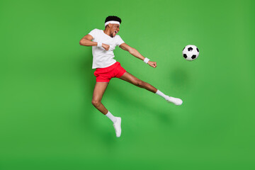 Fototapeta na wymiar Full length photo of funky strong dark skin guy dressed sport outfit jumping playing football isolated green color background