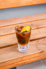 Espresso tonic with ice in a highball glass garnished with an orange zest, on a wooden backdrop