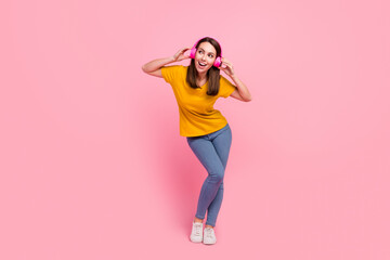 Fototapeta na wymiar Photo of cute excited young lady wear yellow t-shirt listening music looking empty space isolated pink color background