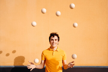 Agile man juggling balls near colorful wall