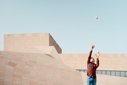 Young man juggling balls near modern building