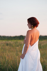 Fototapeta na wymiar Charming caucasian woman in a field at sunset in summer back view