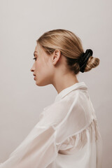 Elegant young blonde in white silk shirt and black hair scrunchie, with trendy hairstyle, turning...