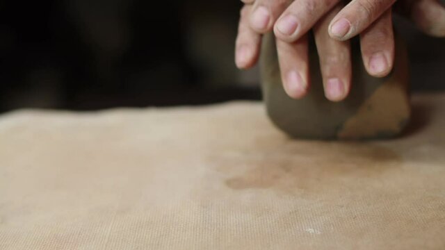 Male hands crumple and roll out piece of clay on table, front view, closeup. Potter prepares clay for processing on table