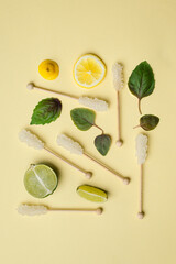 Crystallized white sugar on wooden stick, basil leaves, lemon and lime slices on a light sand-colored background. The concept  layout of the ingredients of a fragrant tea party