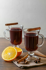 Mulled wine in glass cups with cinnamon and oranges on a wooden table.