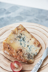 large piece of stilton cheese is lying on a wooden board. Delicacy cheese with blue mold stilton with grapes.