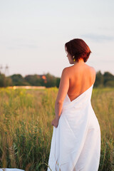 Fototapeta na wymiar Charming caucasian woman in a field at sunset in summer back view
