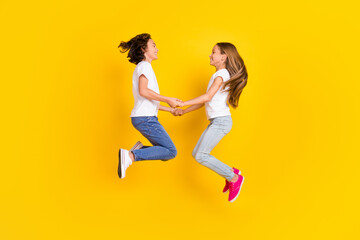 Fototapeta na wymiar Full length body size view of two nice cheerful carefree kids jumping holding hands isolated over bright yellow color background