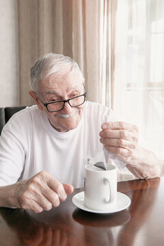 old man with glasses is making a tea bag. A man of 88 years old drinks tea sitting at the table. old pensioner is happy with life