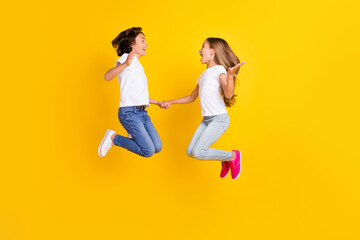 Full length body size view of two nice cheerful ecstatic kids jumping having fun rejoicing isolated over bright yellow color background