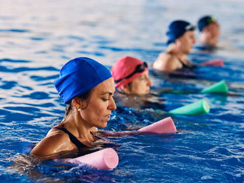 Company of people doing exercise with aqua noodles in pool