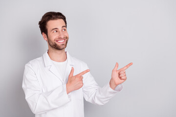 Photo of pretty dreamy young guy doctor workwear looking pointing empty space smiling isolated grey color background