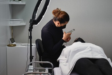 Cosmetologist taking photo of client during beauty procedure