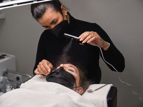 Cosmetician using eyelash steamer in salon