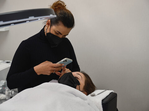 Beautician taking photo of client during eyelashes treatment procedure