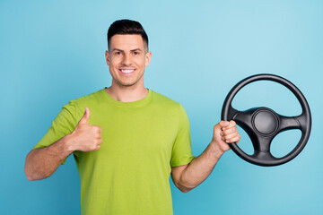 Photo of brunette haired young man make thumb up hold hand steering wheel isolated on blue color...