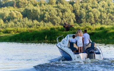 A man, a woman, a child, are floating in a boat with a motor on the river