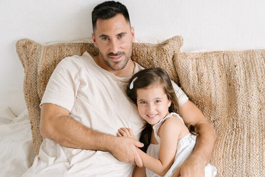 Loving father sitting with little daughter on bed at home