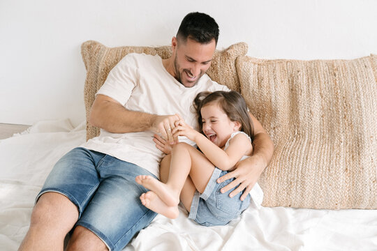 Loving father tickling little daughter on bed at home