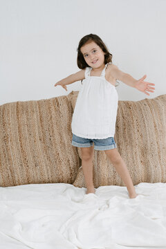 Happy girl standing on bed looking at camera in room at home