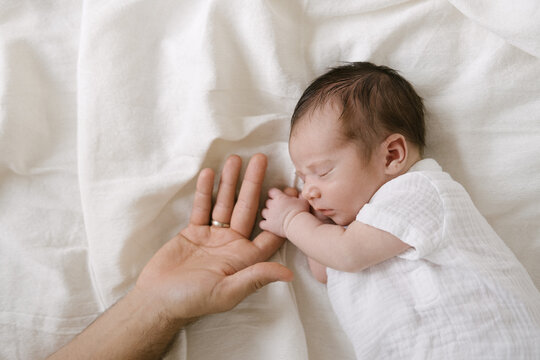 Sleeping newborn holding finger of crop parent