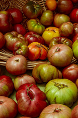 green, red, and yellow heirloom tomatoes spilling from woven basket table display at farmer's market in California