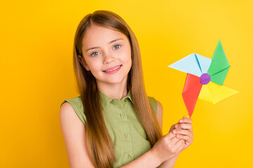 Obraz na płótnie Canvas Photo portrait schoolgirl wearing green shirt smiling playing with windmill isolated vivid yellow color background