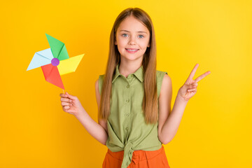 Photo of sweet blond little girl hold toy show v-sign wear khaki blouse isolated on yellow color...
