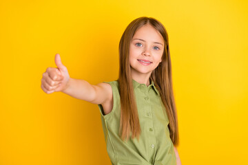 Photo of optimistic blond small girl thumb up wear khaki blouse isolated on yellow color background