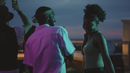 Handheld slowmo shot of happy young black man and woman laughing and dancing together at rooftop party on summer evening