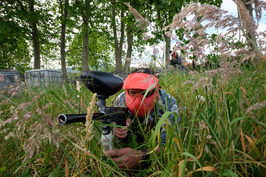 Anonymous paintball player aiming at enemies hiding in grass