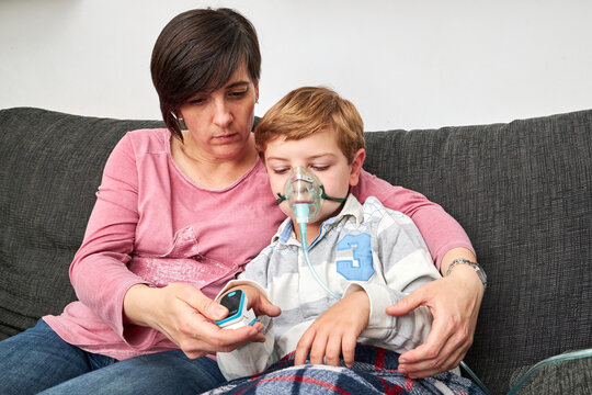 Mother using pulse oximeter on finger of child in oxygen mask