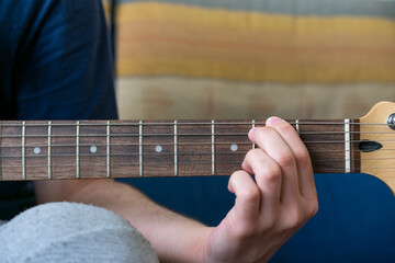 Front-view of an unrecognizable man playing an electric guitar, with his hand on the neck of the...