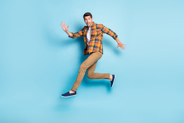 Fototapeta na wymiar Photo of pretty friendly young guy dressed plaid shirt smiling jumping high running isolated blue color background