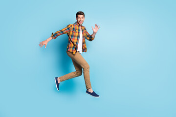 Fototapeta na wymiar Photo of sweet excited young guy dressed plaid shirt spectacles smiling jumping high isolated blue color background