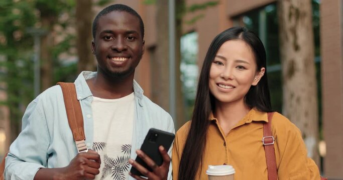 Focused young multiracial college students looking at the smartphone while standing at the street near the university on campus and preparing for exam