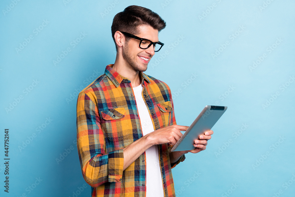 Poster Portrait of attractive cheerful skilled focused guy geek using device surfing web isolated over bright blue color background