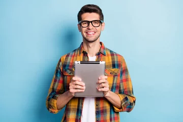 Fotobehang Portrait of attractive cheerful guy geek holding in hands using device app 5g isolated over bright blue color background © deagreez