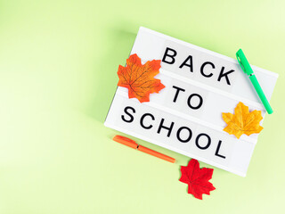 White lightbox with back to school text on green background with autumn leaves and pens