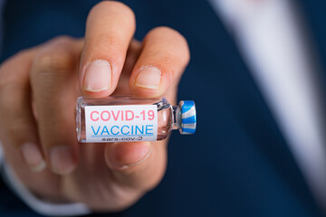 Focus select and blur Foreground Vaccine COVID-19 corona virus and syringe on hand business man in blue suit background. Concept of attentive care.