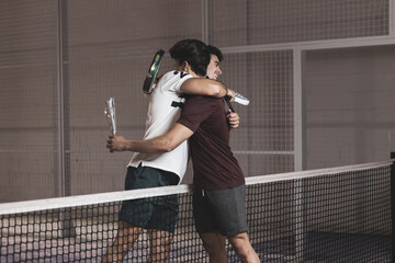two young boys hug each other to celebrate that they have won a paddle tennis match.