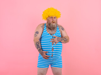 Happy man with yellow wig and swimsuit has stomachache