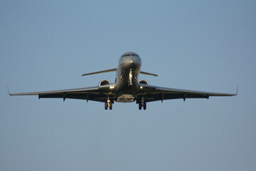 A grey private business jet is landing with its landing gear extended against a gray, clear sky
