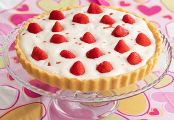 Strawberry tart with white cream on a romantic pink tablecloth decorated with hearts for Valentine's Day