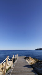 A wooden boardwalk towards the mediterranean sea with a rope handrail, calm sea on a sunny day 