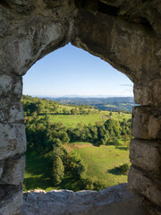 Fototapeta na wymiar Panoramic hilly landscape of Srebrenik village with forests and meadows viewed through stone window of medieval ottoman fortress Srebrenik