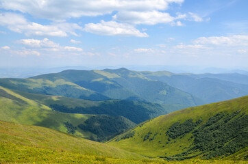 Fototapeta na wymiar Scenic view of green grassy mountain ridge against blue cloudy sky. Carpathian mountains, Ukraine
